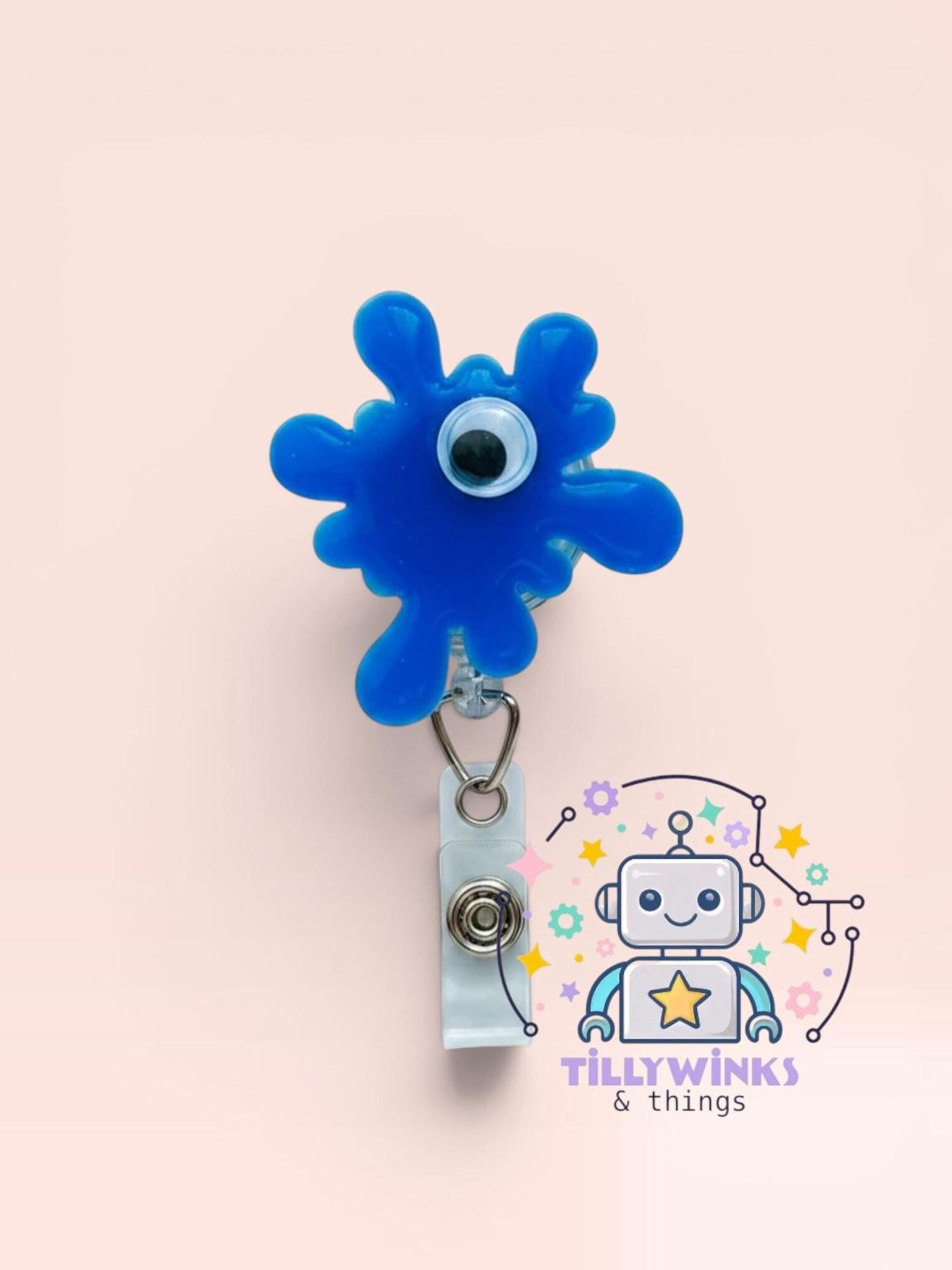 a blue blob-like object with a white eye attached to it, hanging from a white clip. Below the clip, there is a cartoon robot with a star on its head, surrounded by various colorful elements.