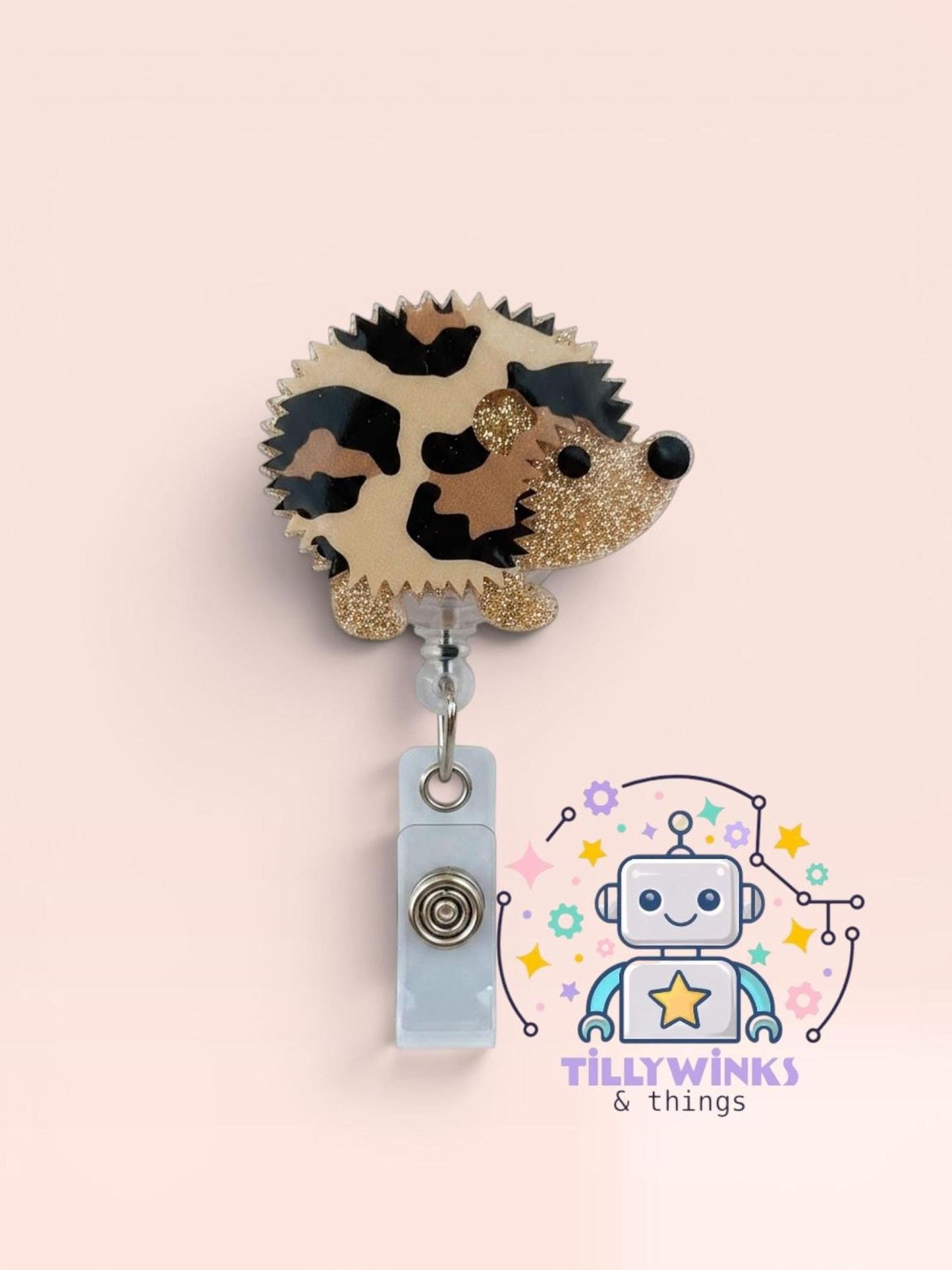 a cute hedgehog-shaped badge with a clear plastic tag hanging from it, and a robot-themed logo for a business called "Tillywinks & things" in the background.