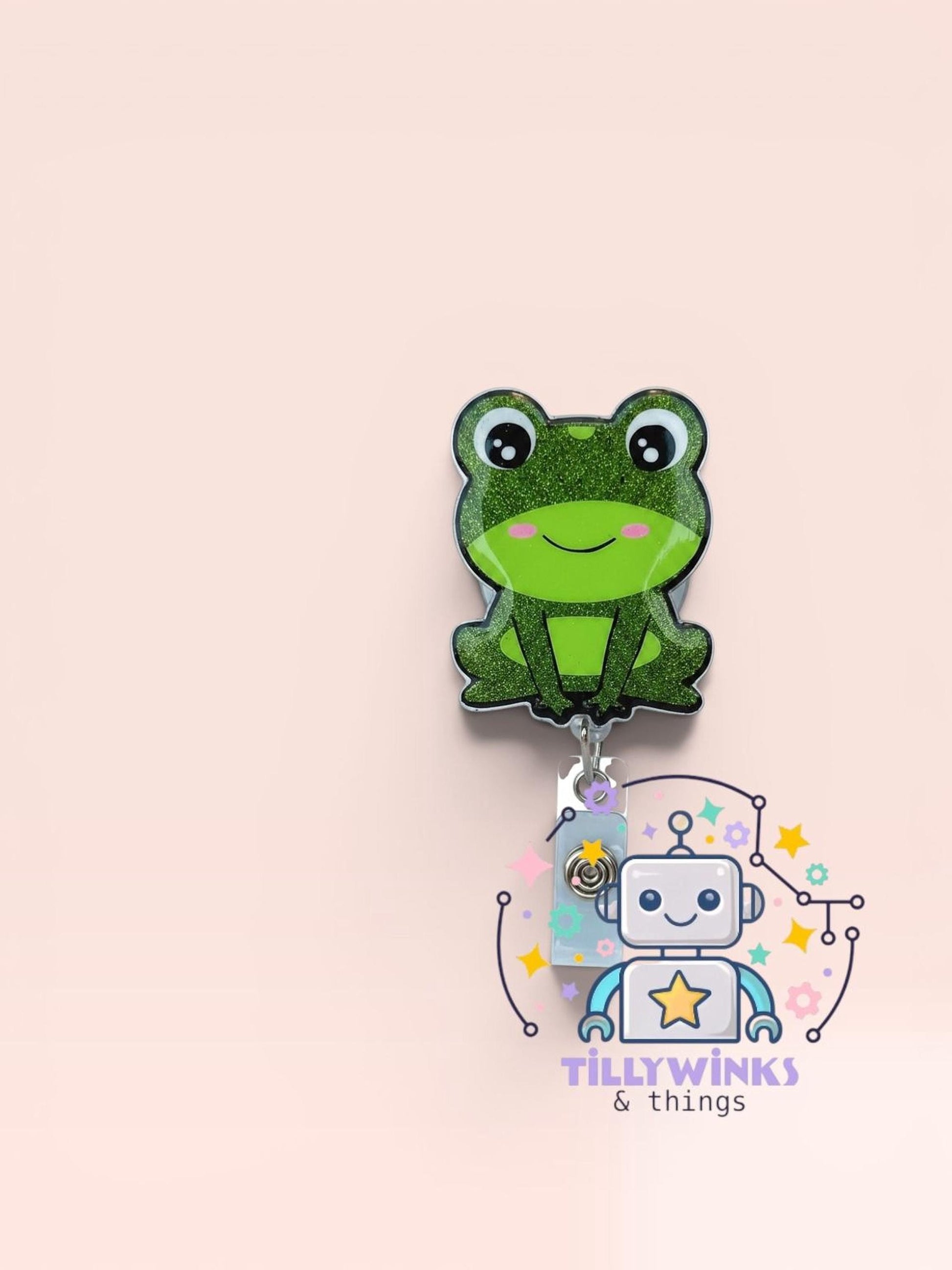 A green frog-shaped charm with a robot-like design is displayed against a light pink background.