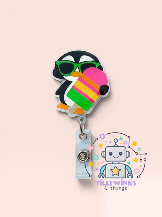 A colorful penguin-shaped badge holder with a popsicle-shaped handle, featuring a robot-like character and a "Tillywinks & things" logo.