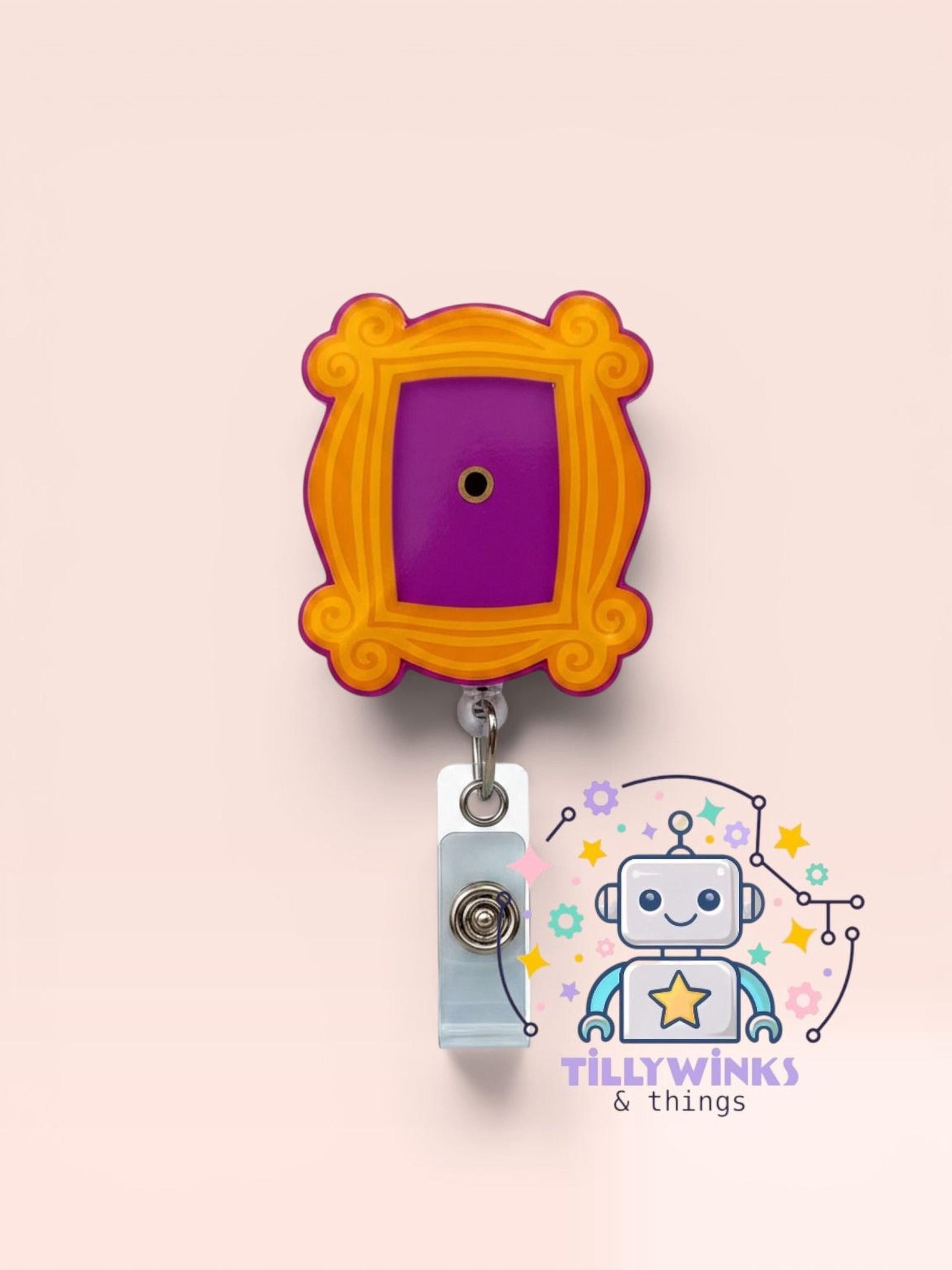 a colorful lanyard with a purple frame and an orange border, hanging on a light pink background. There is also a robot-like character with a star on its head, and the text "Tillywinks & things" is visible in the image.