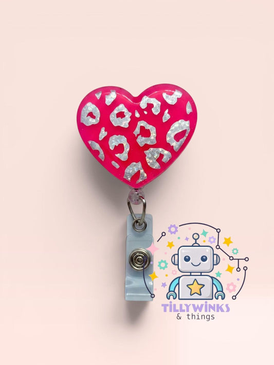 a pink heart-shaped badge holder with a leopard print pattern, attached to a gray clip. Below the heart-shaped badge holder, there is a logo for "Tillywinks & things", which appears to be a brand or company logo.