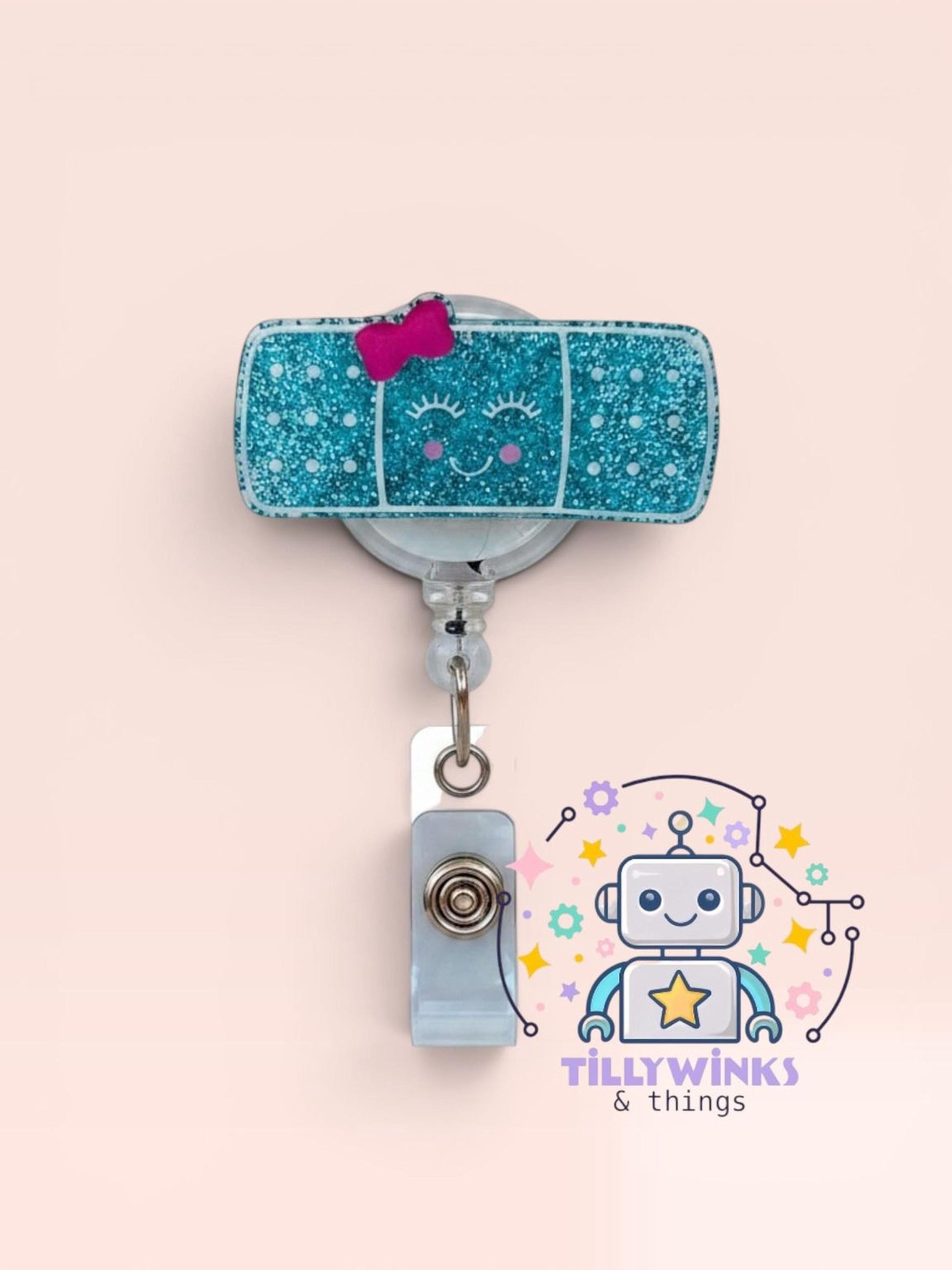 a glittery blue band-aid with a pink bow, attached to a silver clip, and a robot-themed badge with a star and text.